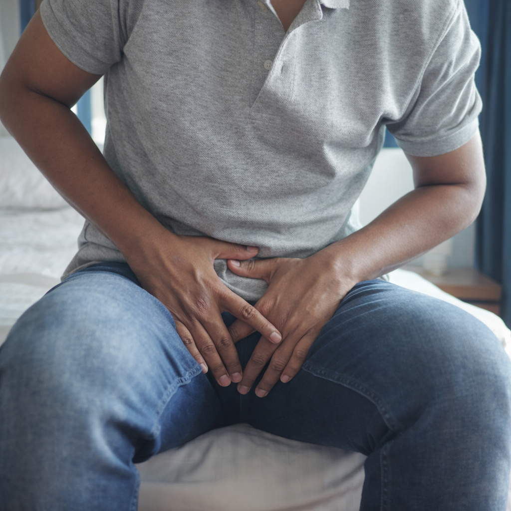 Man experiencing lower abdominal and testicular pain while sitting on a bed